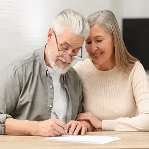 Senior couple smiling while signing a will or estate plan; securing their financial legacy.